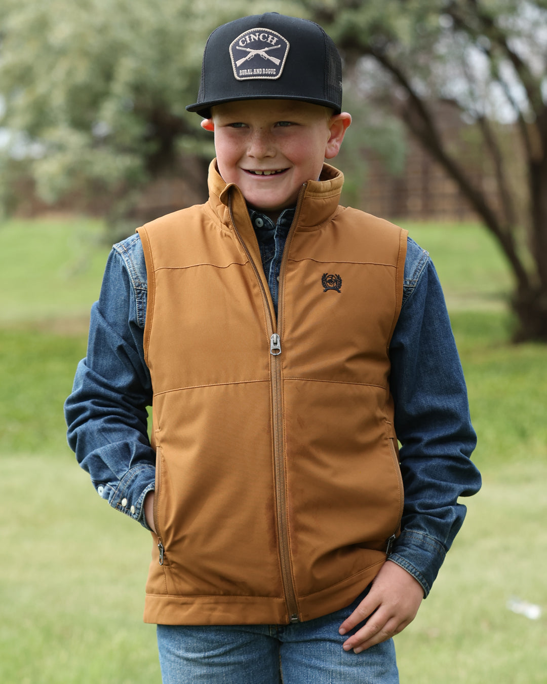 Child wearing a brown vest and blue jacket outdoors